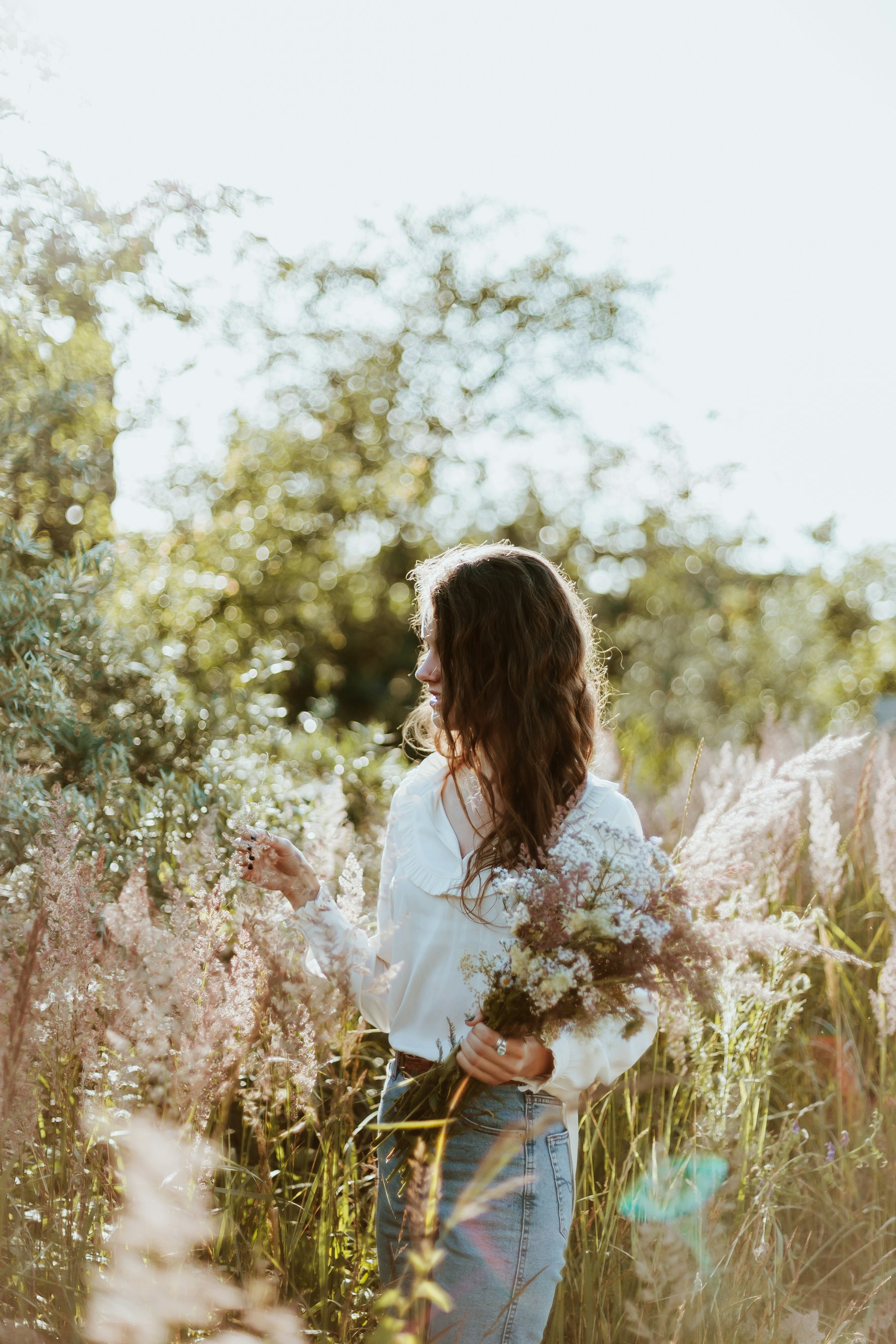 A woman gathering wildflowers in a sunlit meadow